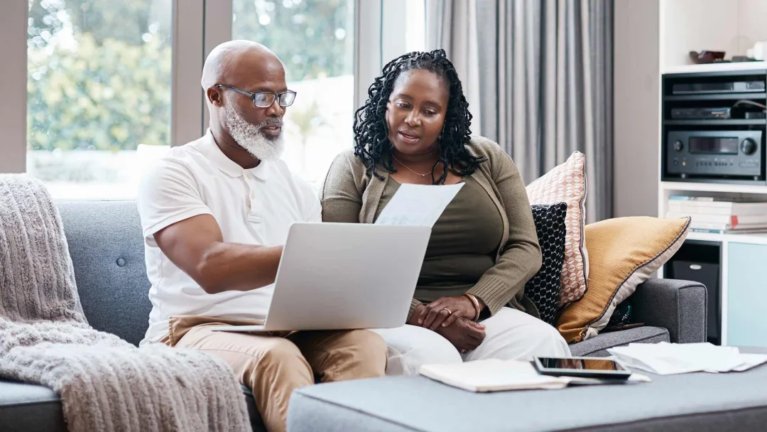 Man and woman reviewing paperwork with computer on lap