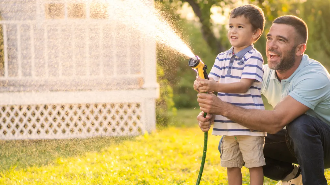 A Father and Son Spray a Garden Hose in the Front Yard as They Laugh