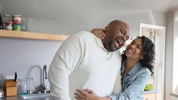 A couple hugging each other while cooking on the kitchen