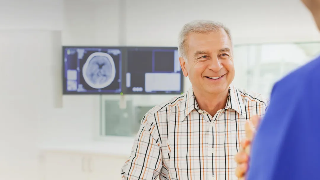Man speaking with a doctor with imaging results on a screen behind him