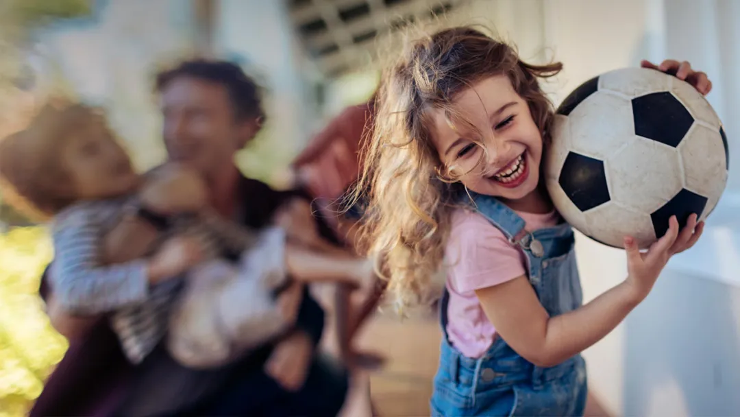 Young girl running with her family and carrying a soccer ball
