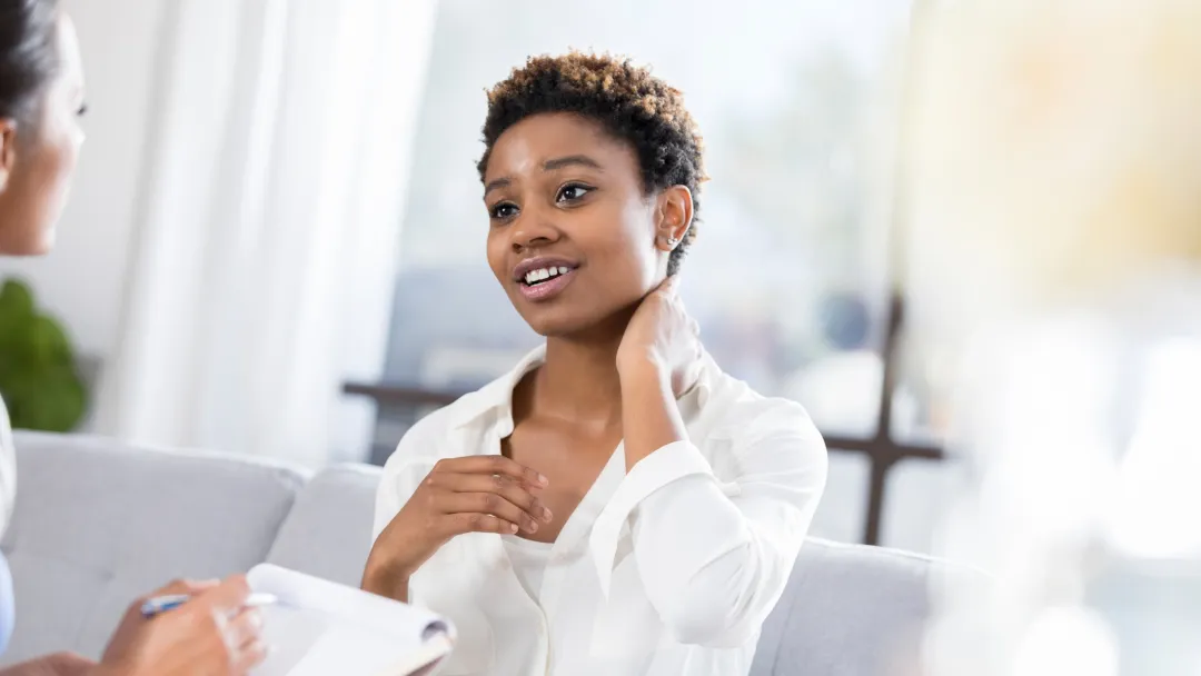 A young woman rubs her neck as she talks to a nurse