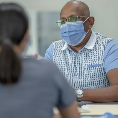 A Health Provider Has a Conversation with a Patient in a Clinic Setting While Wear a Mask