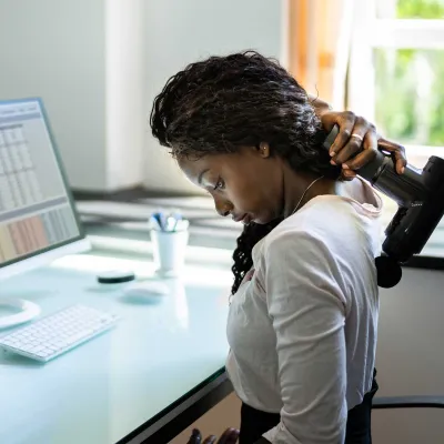 A woman using a massage gun on her back