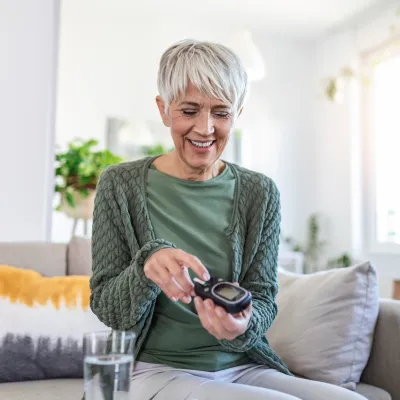 A Senior Woman Smiles as She Checks Her Blood Sugar Level.