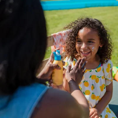 A Mother Applies Sunscreen to Her Smiling Daughter on a Bright Summer Day