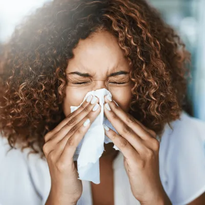 A Woman Sneezes into a Tissue at Home