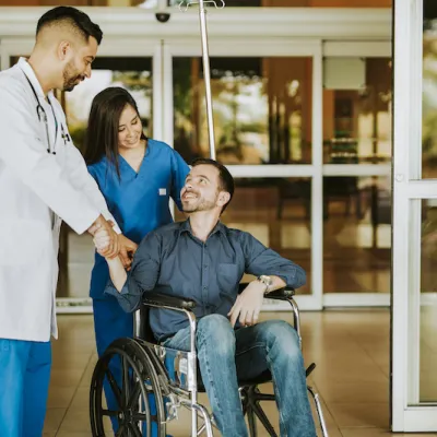 Doctor shaking hands with man as he leaves hospital in a wheelchair