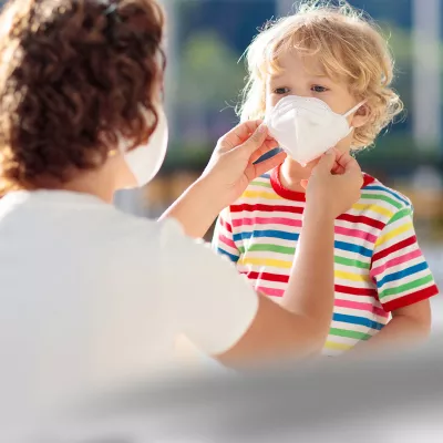 A mom helps her son position his face mask.