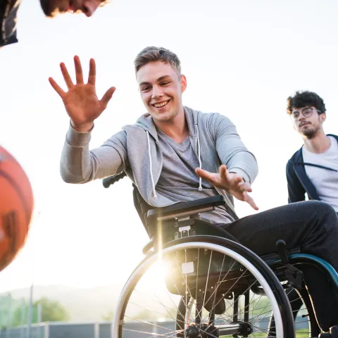 Older teens playing basketball one of which is in a wheelchair 