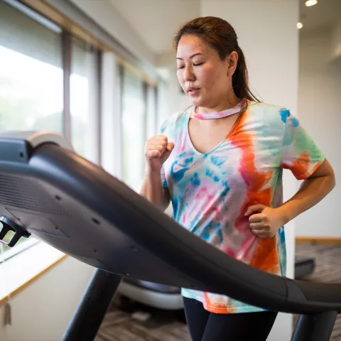 A Woman Jogs on a Treadmill in Front of a Window Overlooking Her Backyard