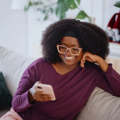 A Woman Smiles as She Reads Her Cell Phone on the Couch at Home.