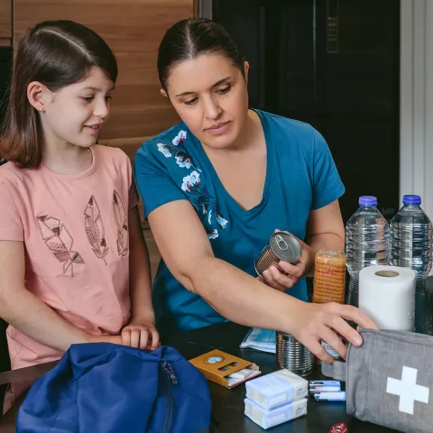 A Mother Looks Over a First Aid Kit with Her Daughter on the Kitchen Table.