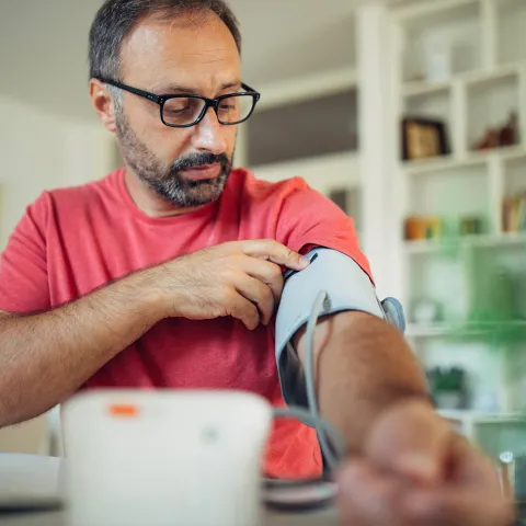 A Middle Aged Man Wearing Glasses Puts on a Blood Pressure Cuff to Take His Blood Pressure.