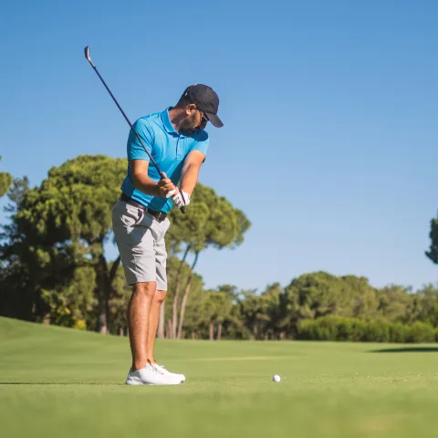 A Man Playing Golf with His Club in the Back Swing of His Approach to the Green.