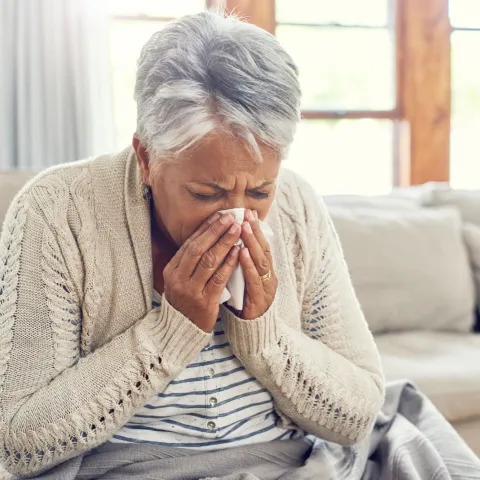 A Senior Woman Blows Her Nose from Seasonal Allergies.