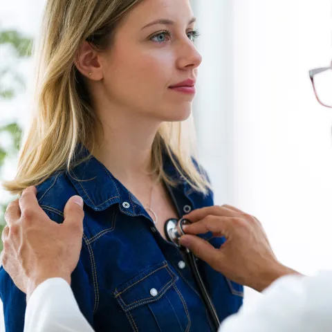 Doctor listening to woman's heart, a hand on her shoulder and a stethoscope 