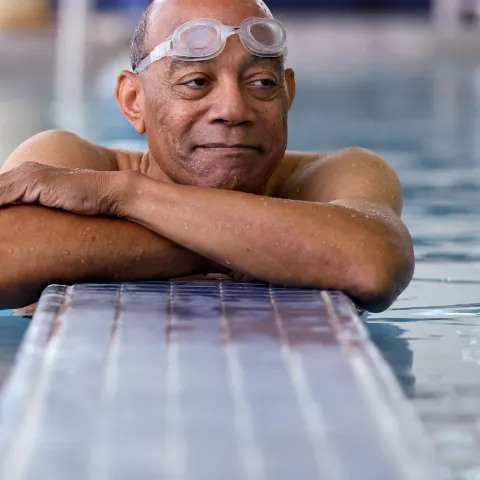 Elderly black man with goggles in a swiming pool.