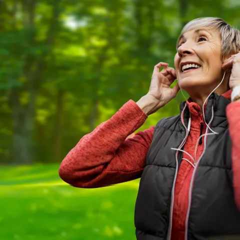 Older woman wearing earbuds outdoors.