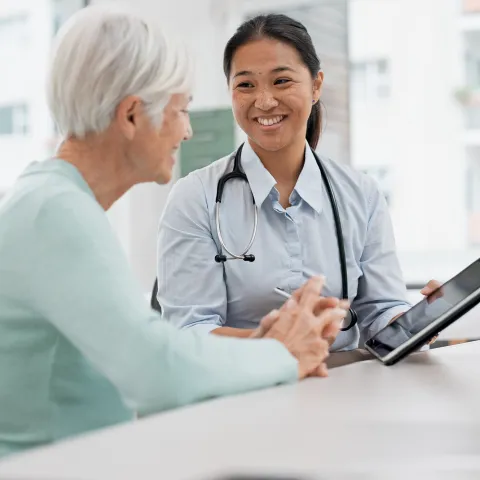 A Physician Smiles While She Goes Over a Patient's Chart With Her on a Tablet