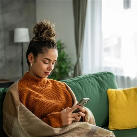 Woman sitting on her green couch and looking at her phone.