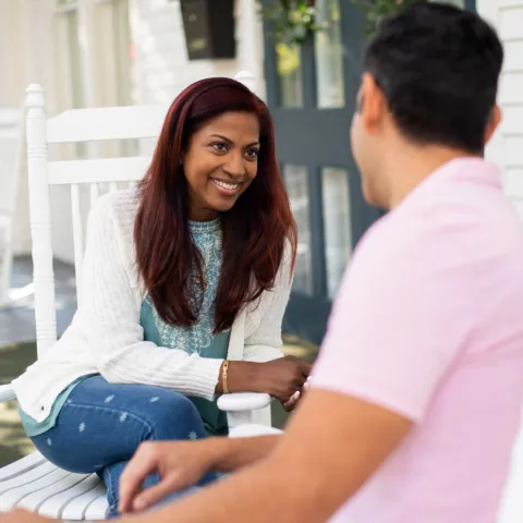 A young hispanic couple sit in rocking chairs on the porch together.