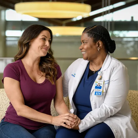 A woman holds hands with her physician and smiles
