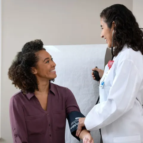 A young woman smiles at her doctor while getting her blood pressure measured.