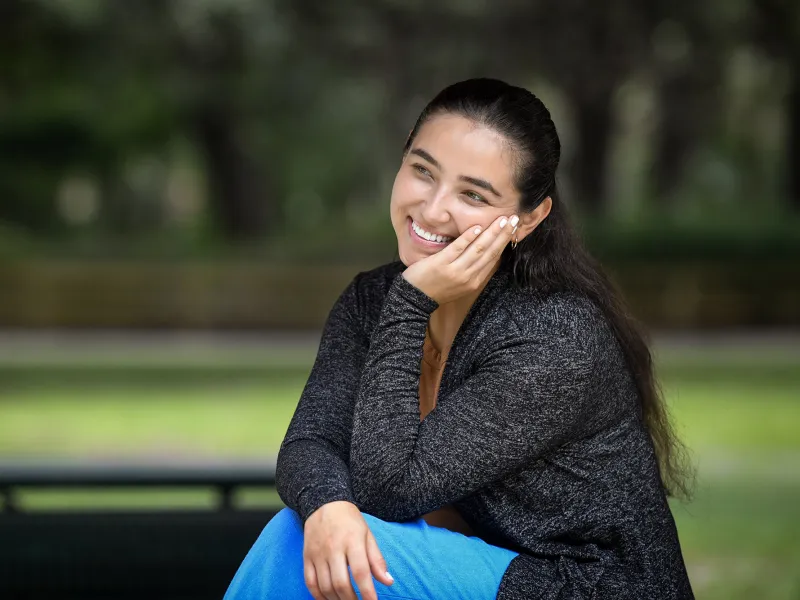 A smiling woman sits on a park bench.