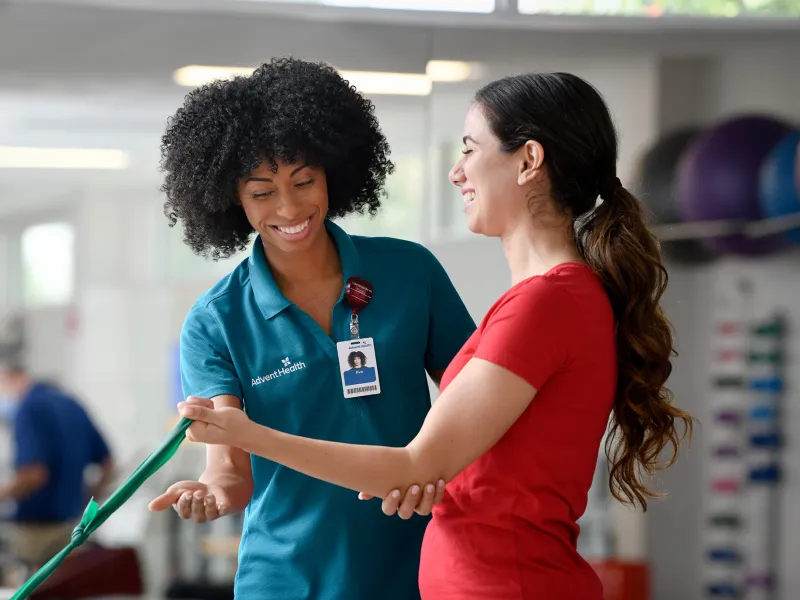 Physical Therapist guiding a woman patient through an exercise to strengthen arm.