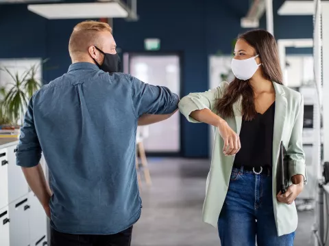 co-workers elbowing hello in the office while wear facemasks