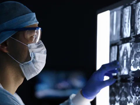 A Doctor, in Full Scrubs and Face Mask, Looks Over His Patient's Scans