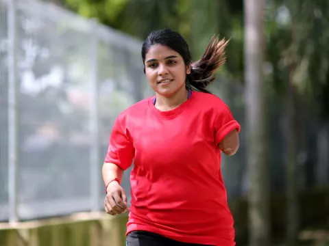 A Teenage Girl with One Lower Arm Runs in a Park.