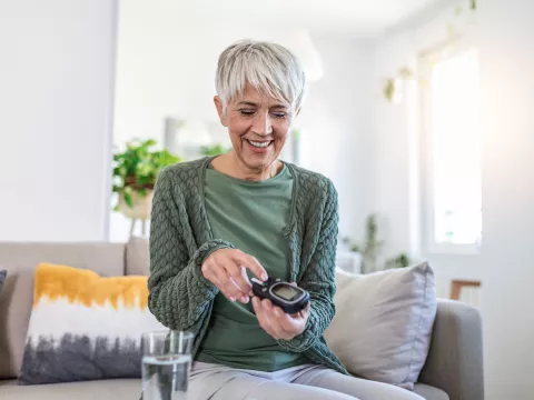 A Senior Woman Smiles as She Checks Her Blood Sugar Level.