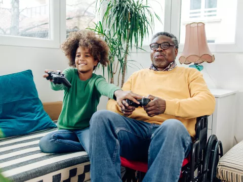 A Grandfather in a Wheelchair Plays Video Games with His Grandson who is Teaching Him How To Play.