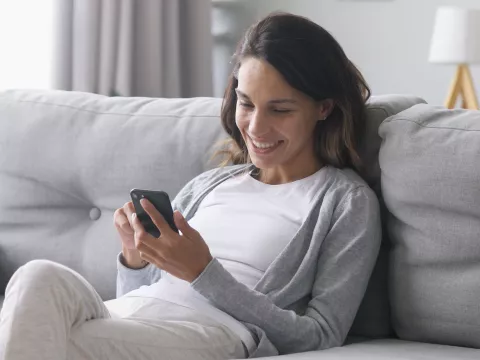 A Woman Sits on Her Couch and Uses Her Smartphone.