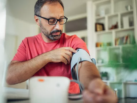 A Middle Aged Man Wearing Glasses Puts on a Blood Pressure Cuff to Take His Blood Pressure.