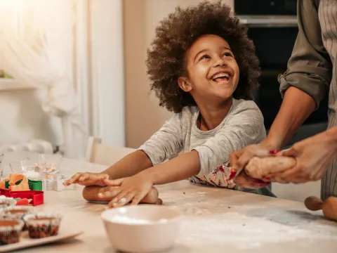 A Young Child Helps Their Parent Roll Out Dough to Make Muffins