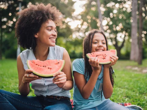 A Mother and Daughter Sit at a Picnic Enjoying Fruit