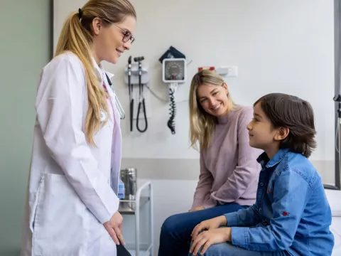 A Mother and Son sit on an Exam Table While They Speak to a Physician