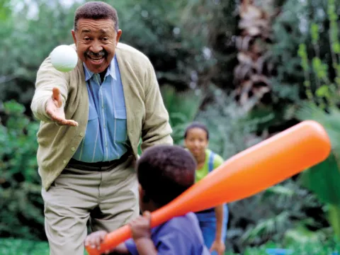 Grandfather playing a game of baseball with his grandson. The mother is behind them.