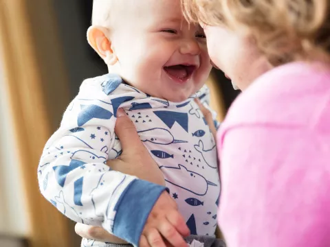 Baby laughing while his mother is holding him.