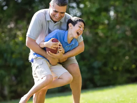 A father and son play football outdoors.