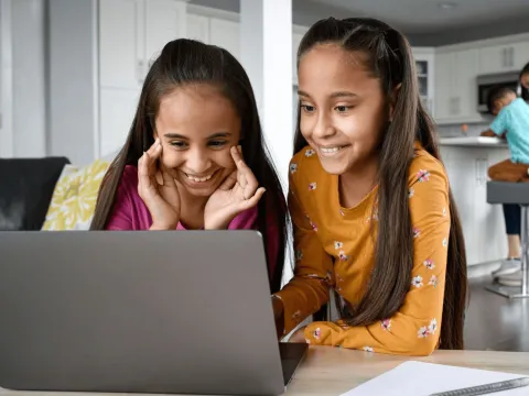 A mother and daughter doing schoolwork on a laptop.