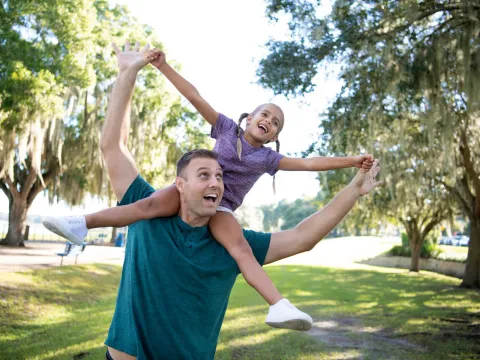 A Father Carries His Daughter on His Shoulders as they Play in a Park