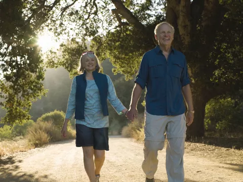 An older Caucasian couple takes an evening walk on a trail.
