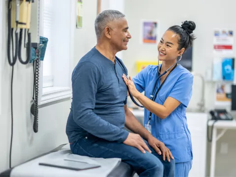 An older Hispanic man gets examined by a nurse.