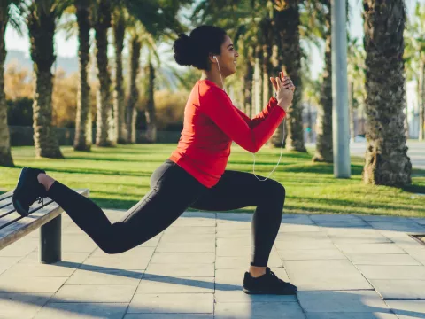 A woman doing a lunge outdoors on a bench.