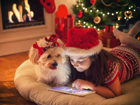 Young girl playing on tablet with dog next to her during the holidays