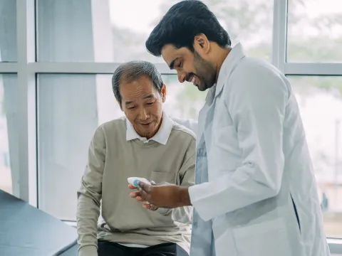 An older patient looking at medical equipment with his physician.